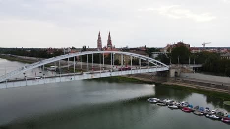 Traffic-on-bridge-over-Tisza-River,-Szeged,-Hungary,-Votive-Church-in-distance,-aerial