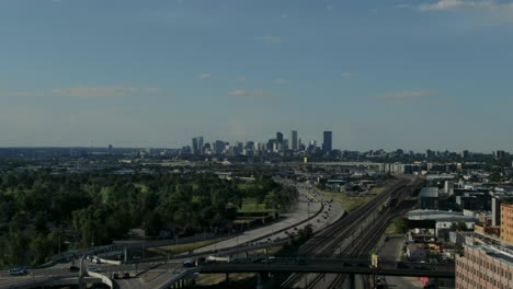 Aerial-drone-panning-shot-over-the-train-tracks-and-highway-with-the-high-skyline-of-Denver-in-the-background
