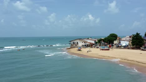 Rotating-aerial-drone-wide-landscape-shot-of-the-tropical-famous-Baia-Formosa-beach-town-in-the-state-of-Rio-Grande-do-Norte,-Brazil-with-fishing-boats,-coastal-homes,-small-waves,-and-surfers