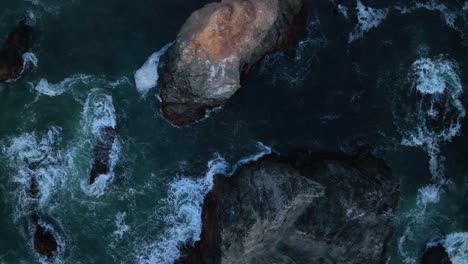 Top-down-rising-aerial-view-of-large-rocks-sitting-off-California's-temperate-coast
