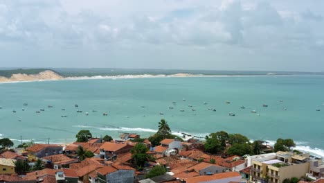 Dolly-in-tilt-down-aerial-drone-shot-flying-over-homes-to-the-famous-Baia-Formosa-beach-in-the-state-of-Rio-Grande-do-Norte,-Brazil-with-fishing-boats,-coastal-homes,-small-waves,-and-surfers