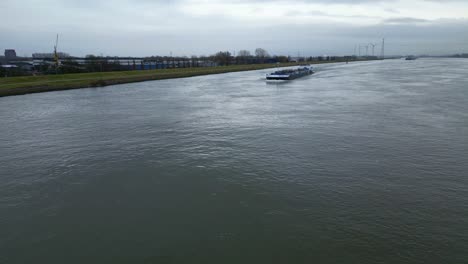Toma-Aérea-Volando-Hacia-Un-Barco-De-Transporte-Interior-Sobre-El-Río-Maas,-Holanda-Del-Sur,-Países-Bajos