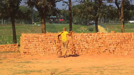 A-brick-worker,-dressed-in-traditional-attire,-carries-and-piles-newly-made-bricks,-showcasing-the-hard-work-in-Asian-brick-making-industry