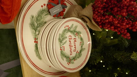 Vertical-video-of-Merry-Christmas-decorative-plates-under-Xmas-tree,-handheld