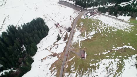 Drone-flying-over-road-in-winter-landscape-in-Switzerland,-following-a-red-car