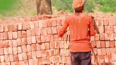 An-efficient-brick-worker-stacks-new-bricks-on-a-pile,-showcasing-tribal-Asian-industry-and-hard-work