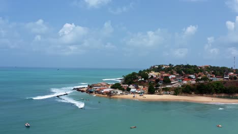 Dolly-in-aerial-drone-wide-shot-of-the-Cacimba-beach-in-the-famous-beach-town-of-Baia-Formosa-in-Rio-Grande-do-Norte,-Brazil-with-fishing-boats,-houses-along-the-coast-and-small-waves
