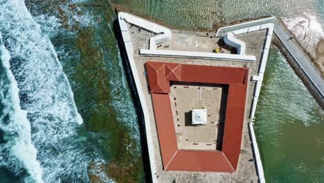 Bird's-eye-top-aerial-drone-shot-of-the-historic-star-shaped-Reis-Magos-fort-built-on-a-reef-with-waves-crashing-into-the-white-walls-in-the-beach-capital-city-of-Natal-in-Rio-Grande-do-Norte,-Brazil