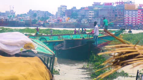 A-busy-Buriganga-river-flows-with-boats,-including-a-trawler-engine-boat,-with-Dhaka-city-visible-in-the-background