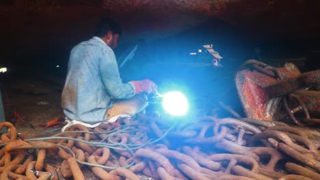 A-dry-dock-worker-welds-a-metal-chain-for-an-anchor-in-the-dark,-creating-sparks-and-dramatic-lighting