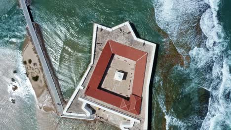 Bird's-eye-top-aerial-drone-shot-of-the-historic-star-shaped-Reis-Magos-fort-built-on-a-reef-with-waves-crashing-into-the-white-walls-in-the-beach-capital-city-of-Natal-in-Rio-Grande-do-Norte,-Brazil