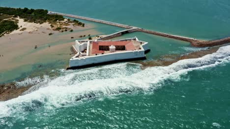 Tilt-down-aerial-drone-shot-flying-over-the-historic-star-shaped-Reis-Magos-military-fort-with-waves-crashing-into-the-white-walls-in-the-beach-capital-city-of-Natal-in-Rio-Grande-do-Norte,-Brazil
