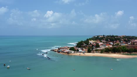 Aerial-drone-wide-shot-of-the-Cacimba-beach-in-the-famous-beach-town-of-Baia-Formosa-in-Rio-Grande-do-Norte,-Brazil-with-fishing-boats,-houses-along-the-coast,-small-waves,-and-sea-birds-flying-around