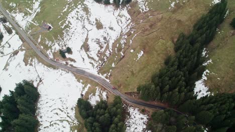 Top-down-aerial-drone-view-of-car-driving-on-road-in-winter-with-snow-in-Switzerland