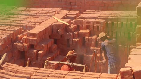 Local-Indian-workers-stacking-and-collecting-dusty-red-bricks-for-community-building-structures,-green-lens-flare-shot