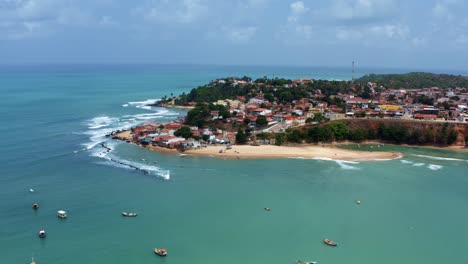 Right-trucking-aerial-drone-wide-shot-of-the-Cacimba-beach-in-the-beach-town-of-Baia-Formosa-in-Rio-Grande-do-Norte,-Brazil-with-fishing-boats,-coastal-houses,-small-waves,-and-sea-birds-flying-around