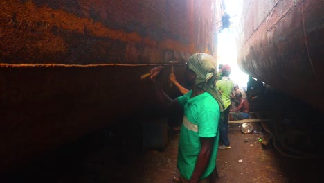 A-rusty-ship-hull-being-hammered-in-dry-dock,-an-industrial-process-to-maintain-the-vessel's-seaworthiness