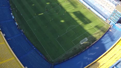 Toma-Aérea-De-Arriba-Hacia-Abajo-Que-Muestra-Al-Equipo-De-Boca-Juniors-Jugando-Fútbol-En-El-Estadio-Durante-El-Día-Soleado---Estadio-Alberto-José-Armando,buenos-Aires