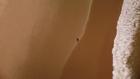 Surfer-Silhouette-Mit-Surfbrett-Am-Sandstrand-Von-Peniche,-Luftaufnahme-Von-Oben-Nach-Unten