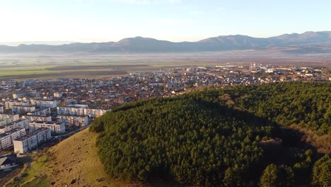 Aerial-footage-of-the-town-of-Sopot,-Bulgaria,-and-the-pine-forest-located-next-to-it,-during-sunrise