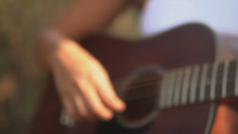 Close-up-push-out-shot-in-slow-motion-of-a-female-hand-strumming-the-guitar-during-sunset