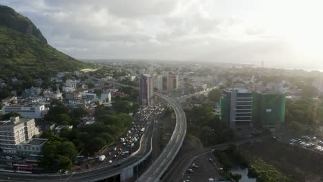 Descending-aerial-shot-of-traffic-in-Port-Louis-with-green-mountains-during-cloudy-day