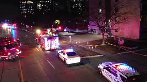 Aerial-shot-of-firetruck-and-police-cars-parked-in-front-of-a-bounding-at-night