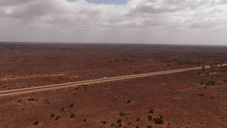 Aerial-view-of-white-camper-van-on-empty-highway-surrounded-by-red-desert-in-Australia-during-cloudy-day