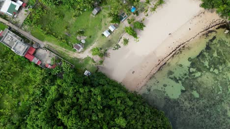 Top-down-Cinematic-Drone-shot-of-hidden-white-sand-beach-and-transparent-ocean-waters-between-lush-palm-tree-covered-mountains