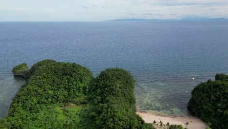 An-aerial-view-of-a-serene-bay-in-Catanduanes-Island,-Philippines,-showcasing-the-beach,-tree-covered-mountains,-and-crystal-clear-ocean