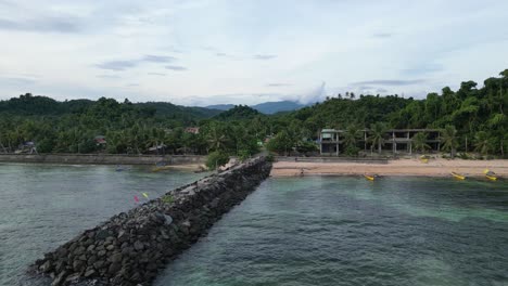 Approaching-Aerial-Overhead-shot-of-picturesque-rocky-breakwater-by-rural-Philippine-village-community