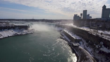 Aerial-pan-of-misty-Niagara-Falls-and-city-skyline-in-snowy-winter