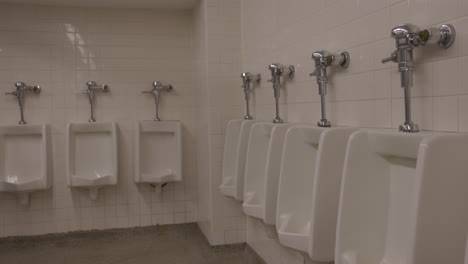 Urinals-in-public-rest-room-washroom-on-white-tile-walls---empty-bathroom