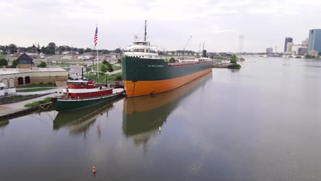 American-flag-wave-near-Great-Lakes-museum-and-industrial-vessel,-aerial-drone-view