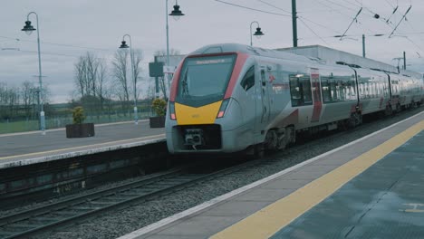 Panning-shot-of-a-commuter-train-leaving-a-station-in-Ely-England-with-a-few-passengers-waiting-for-their-train