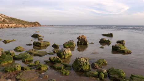 Mossy-boulders-near-Scala-dei-Turchi-in-Argigento,-Sicily-at-sunset-with-water-waves