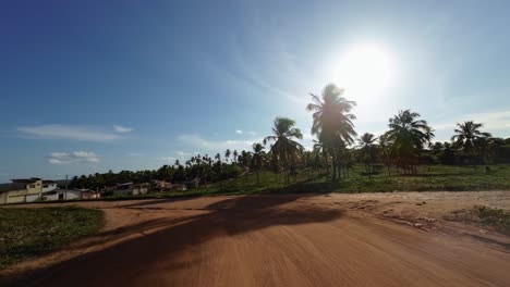 Slow-motion-shot-moving-down-a-small-dirt-road-with-palm-trees-and-a-view-of-the-ocean-from-the-Barra-de-Cunhaú-in-the-small-town-of-Canguaretama-in-Rio-Grande-do-Norte,-Brazil-on-a-summer-day