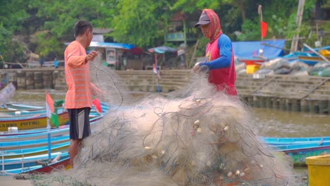 Two-asian-fishermen-rolling-fishing-nylon-net-in-the-harbour-at-day-time---Baron-Beach,-Indonesia