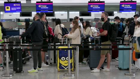 Los-Pasajeros-De-Viaje-Hacen-Cola-Para-Registrarse-En-La-Aerolínea-De-Bandera-De-Tailandia,-Thai-Airways,-Mostrador-De-Recepción-En-El-Aeropuerto-Internacional-De-Hong-Kong