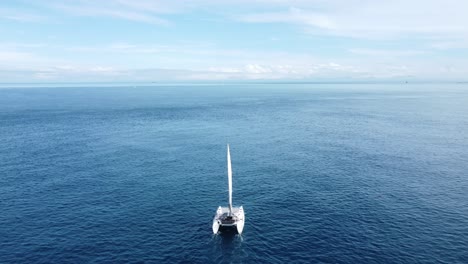 A-small-yacht-slowly-sailing-away-from-the-camera-in-a-still,-calm-ocean