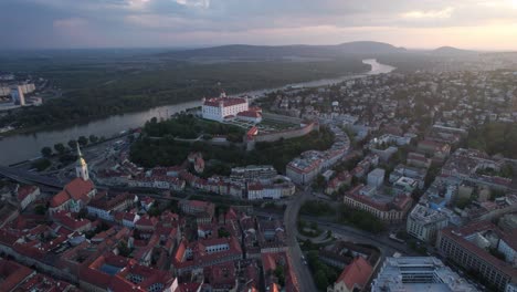 Orbit-Aerial-Shot-of-Bratislava-Castle-or-Bratislavsky-Hrad-Old-Town-At-Sunset,-Danube-River-Waving-Towards-Mountains