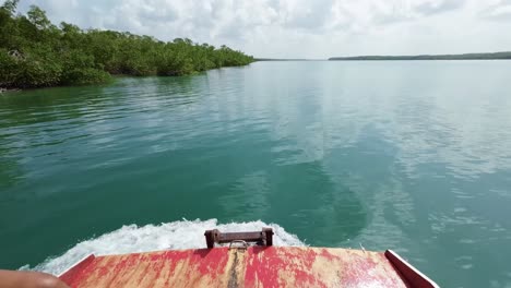 Tilt-up-slow-motion-action-camera-shot-from-aboard-a-small-guide-boat-moving-upstream-on-a-tropical-crystal-clear-turquoise-river-near-the-beach-town-of-Barra-do-Cunhaú-in-Rio-Grande-do-Norte,-Brazil