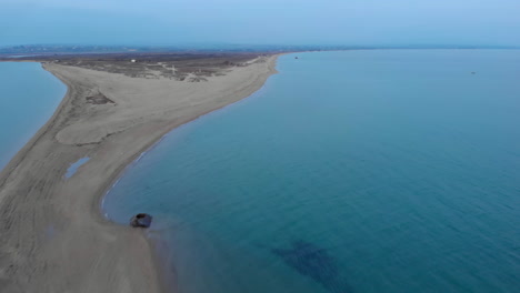 Orbit-Drone-video-over-empty-sand-beach-sea-cape-blue-water-at-sunset-Greece