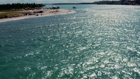 Tilt-up-dolly-in-aerial-shot-flying-over-the-tropical-touristy-Restinga-beach-where-the-large-Curimataú-river-meets-the-sea-near-Barra-do-Cunhaú-in-Rio-Grande-do-Norte,-Brazil-on-a-summer-day