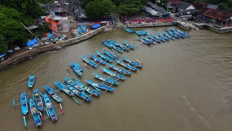Vista-Aérea-De-Barcos-De-Pescadores-Tradicionales-Asiáticos-Amarrados-En-Aguas-Sucias-De-Un-Puerto-En-Yogyakarta,-Indonesia