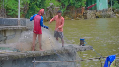 Fishermen-pulling-in-casting-net-from-boat-at-village-dock-after-fishing,-Indonesia