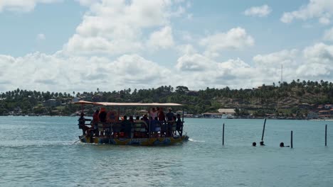 Panning-right-shot-of-a-very-full-transport-boat-full-of-locals-and-tourists-leaving-the-Restinga-beach-sailing-towards-the-Barra-de-Cunhaú-beach-in-Canguaretama-in-Rio-Grande-do-Norte,-Brazil