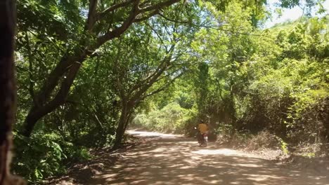 Slow-motion-shot-moving-down-a-winding-small-dirt-road-surrounded-by-tropical-trees-in-the-small-town-of-Canguaretama-near-Tibau-do-Sul-and-Natal-in-Rio-Grande-do-Norte,-Brazil-on-a-summer-day
