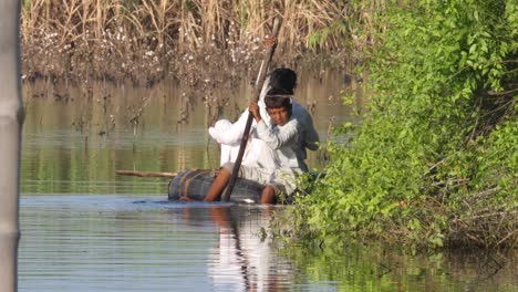 Kind-Schwimmt-Auf-Einem-Großen-Gummireifen-Auf-überflutetem-Land-Und-Manövriert-Mit-Einem-Stock-In-Sindh,-Pakistan