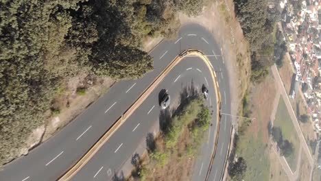 Cars-driving-on-curvy-highway-road-near-city,-vertical-aerial-view